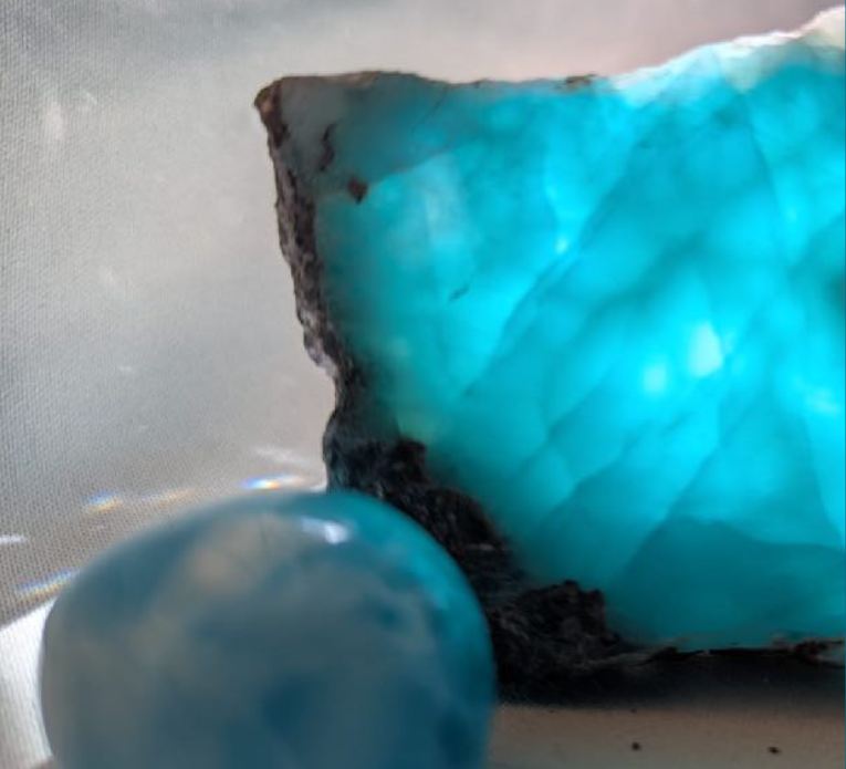 cette image descrit une pierre polie ronde naturellle semi-précieuse larimar ainsi qu'une pierre brute larimar